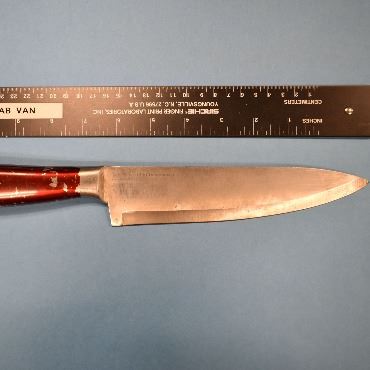 Large kitchen knife lying on a table next to a ruler.