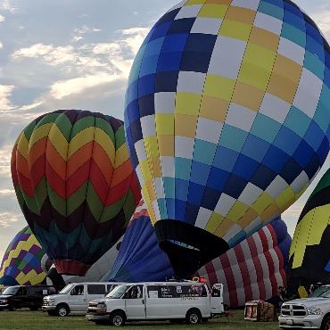 Several colorful hot air balloons inflating with their trucks nearby