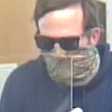 White man with brown hair wearing dark blue hoodie, face mask, and sunglasses