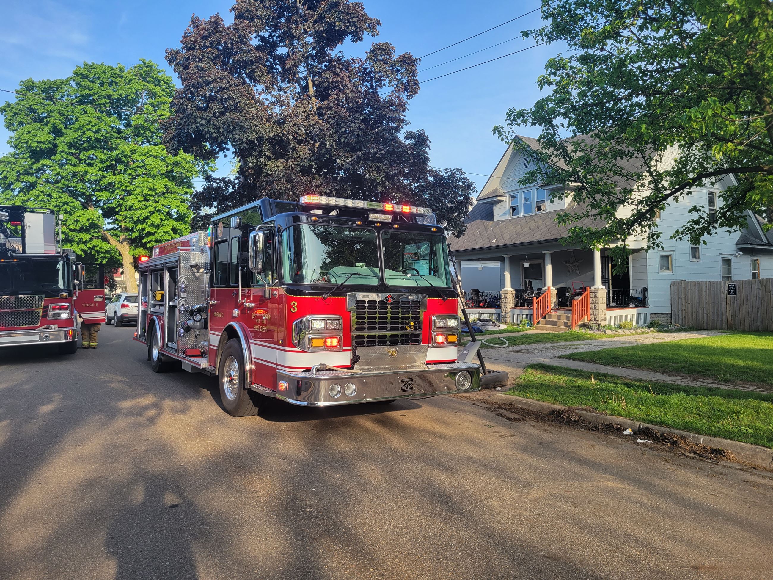 Two fire trucks parked on the street outside a home during daylight.