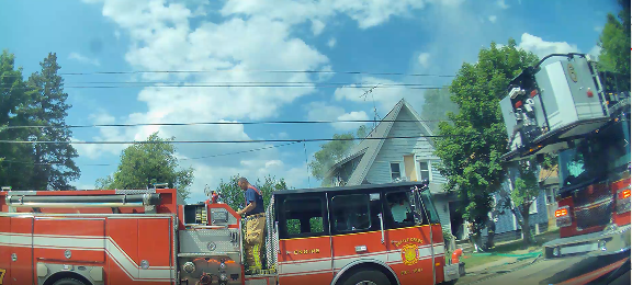 Fire trucks parked on street next to a blue, two-story house.